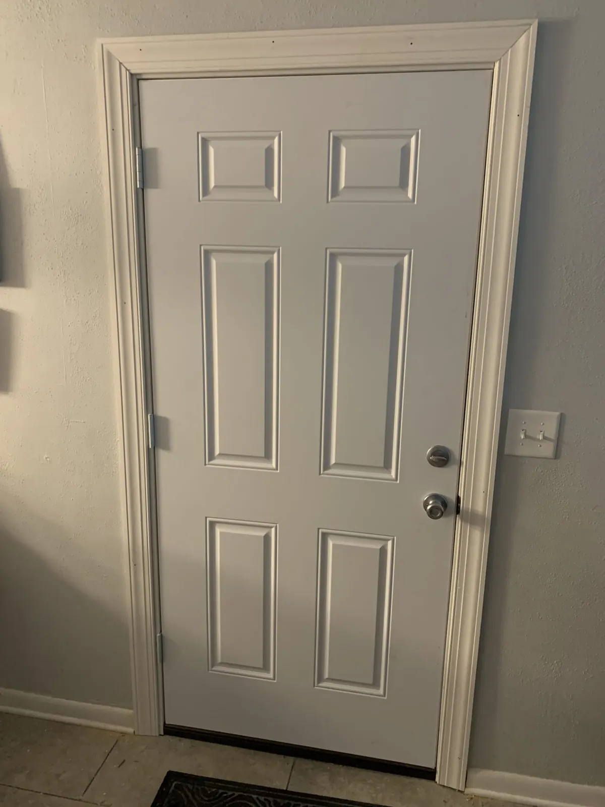 White six-panel entry door with trim and a brushed nickel knob in a home entryway
