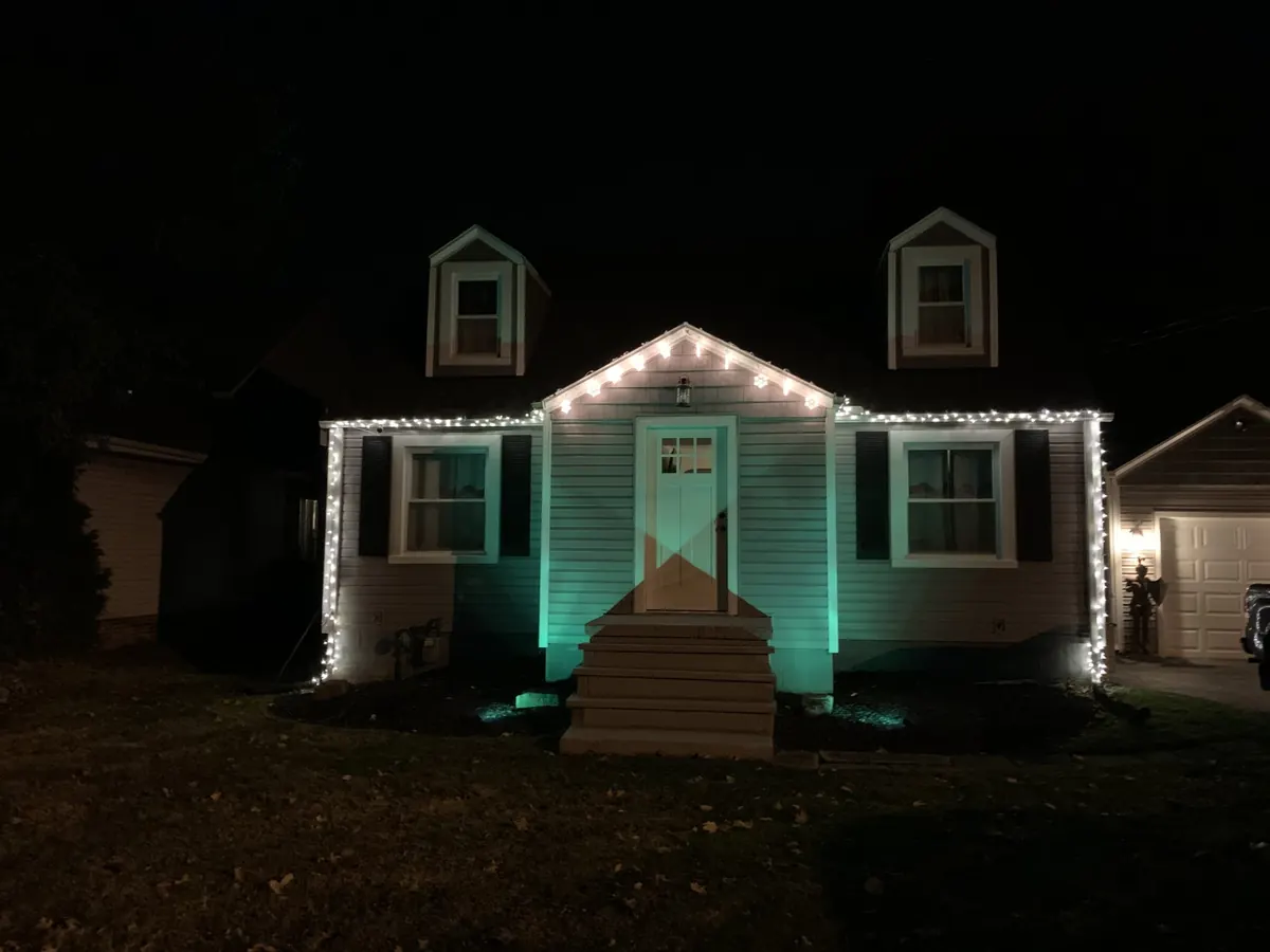 Cape Cod style house with white roof lights and teal uplighting at night