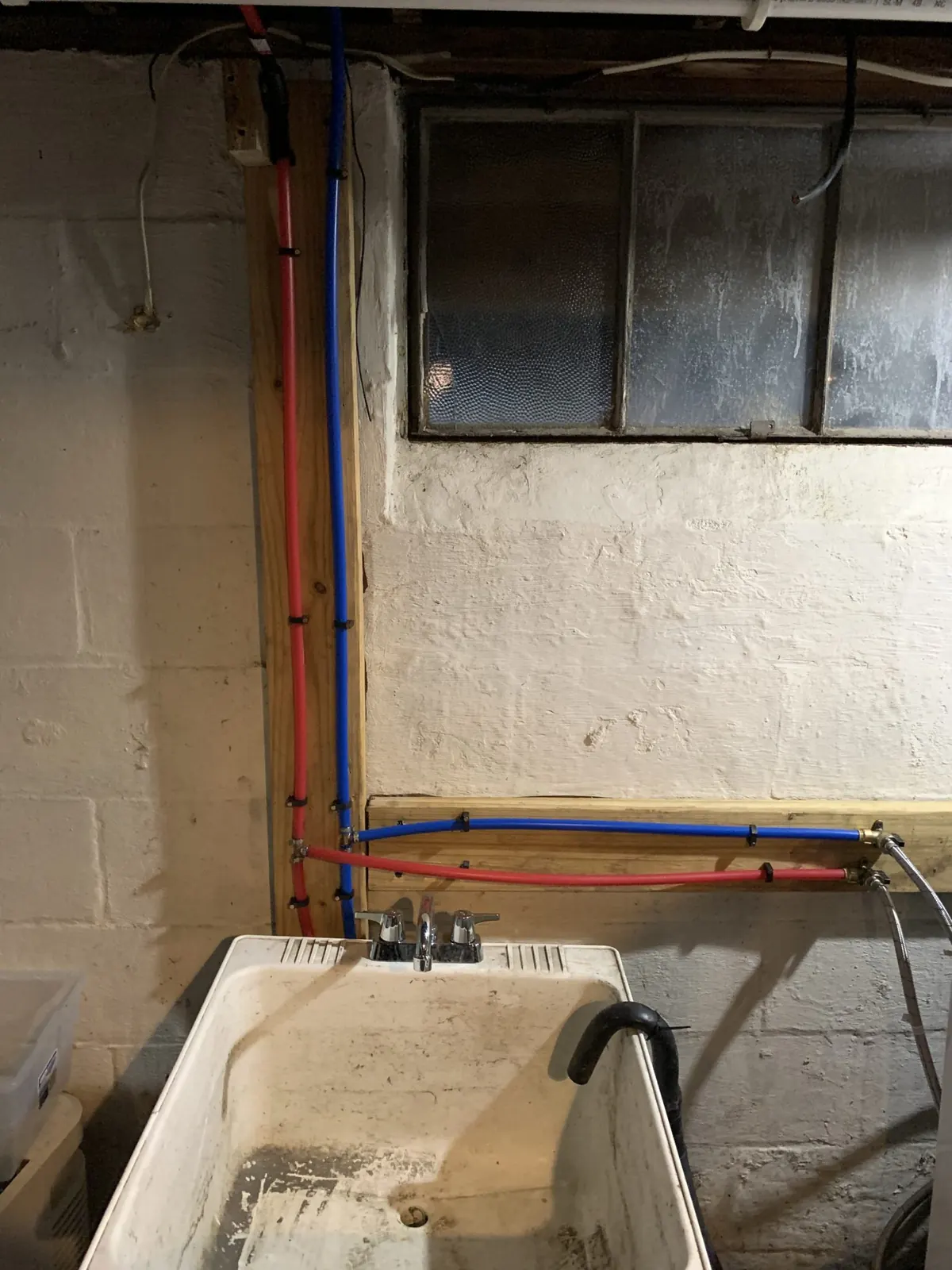 Basement utility sink with red and blue water supply lines run along wood framing by Monthly Upkeep in the Cleveland area