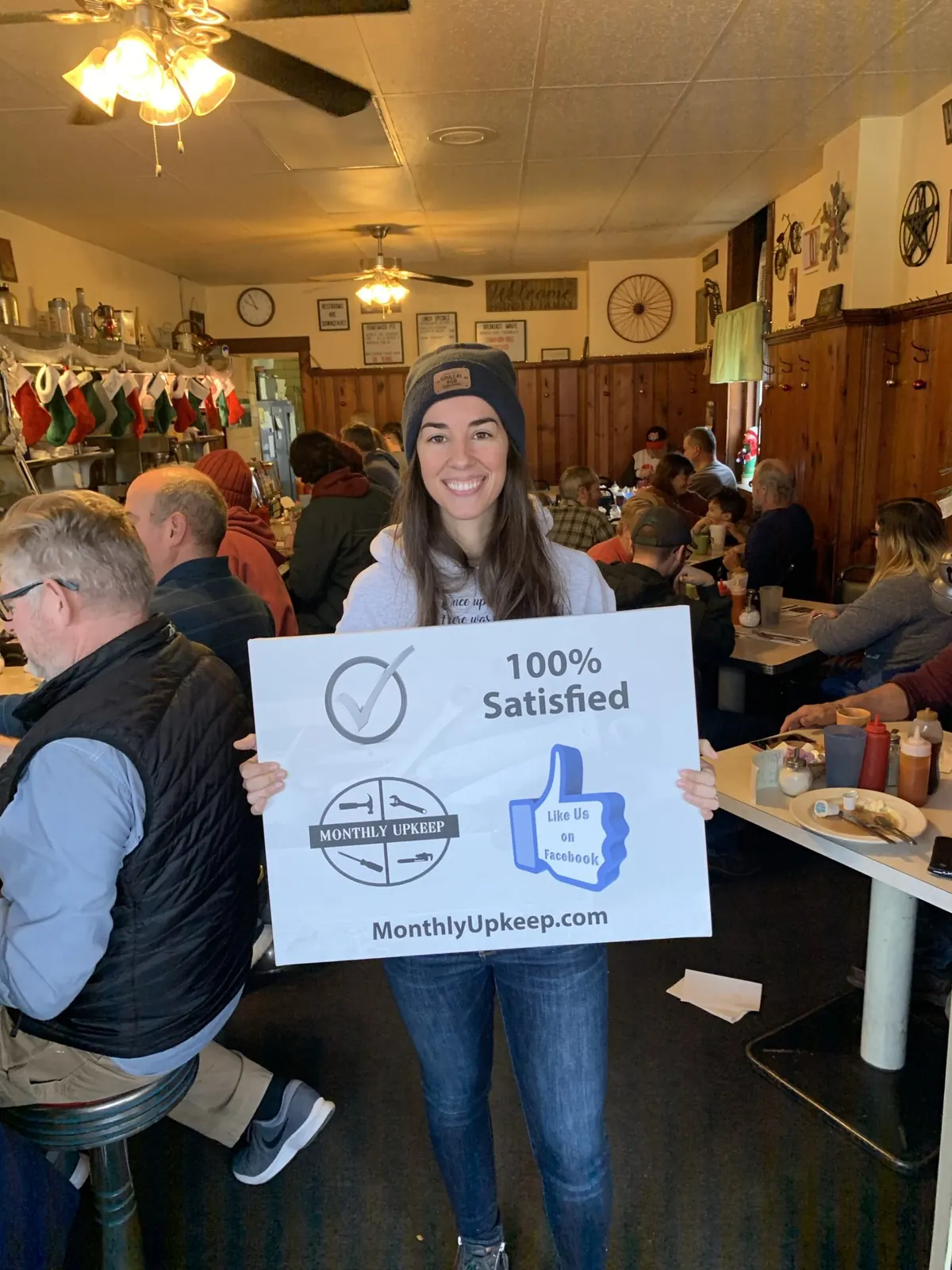 Customer holding a 100% Satisfied Monthly Upkeep sign inside a restaurant