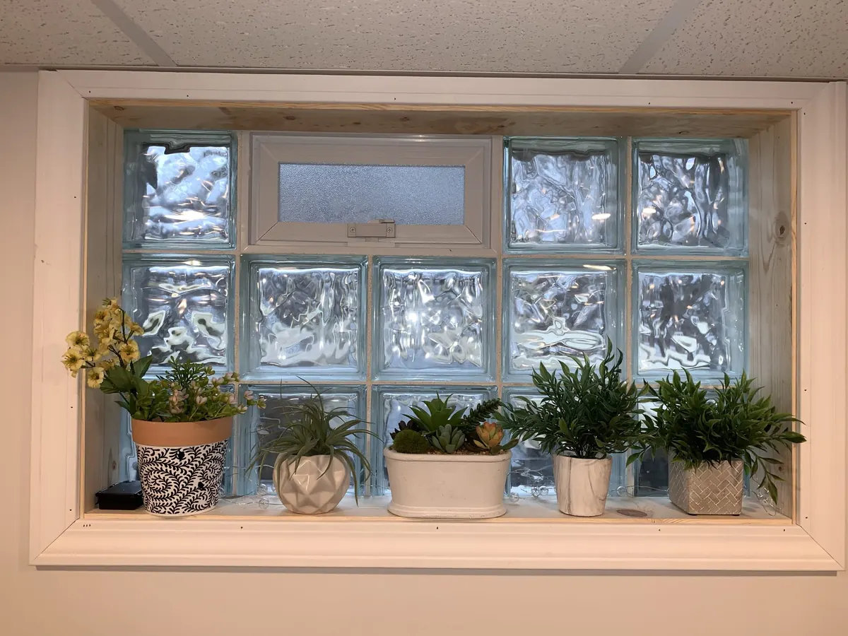 Glass block window with a vented pane and potted plants on the sill by Monthly Upkeep in the Cleveland area
